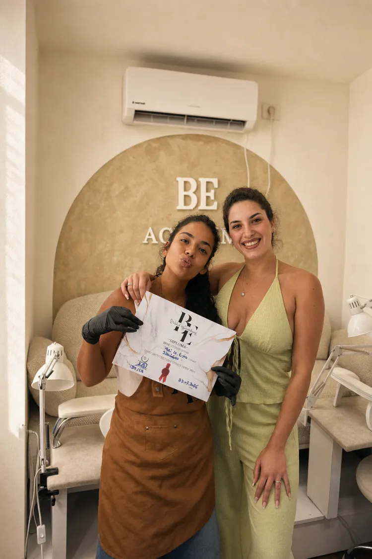 בוגרת בסינר מחזיקה את תעודת הסיום שלה לצד המדריכה שלה